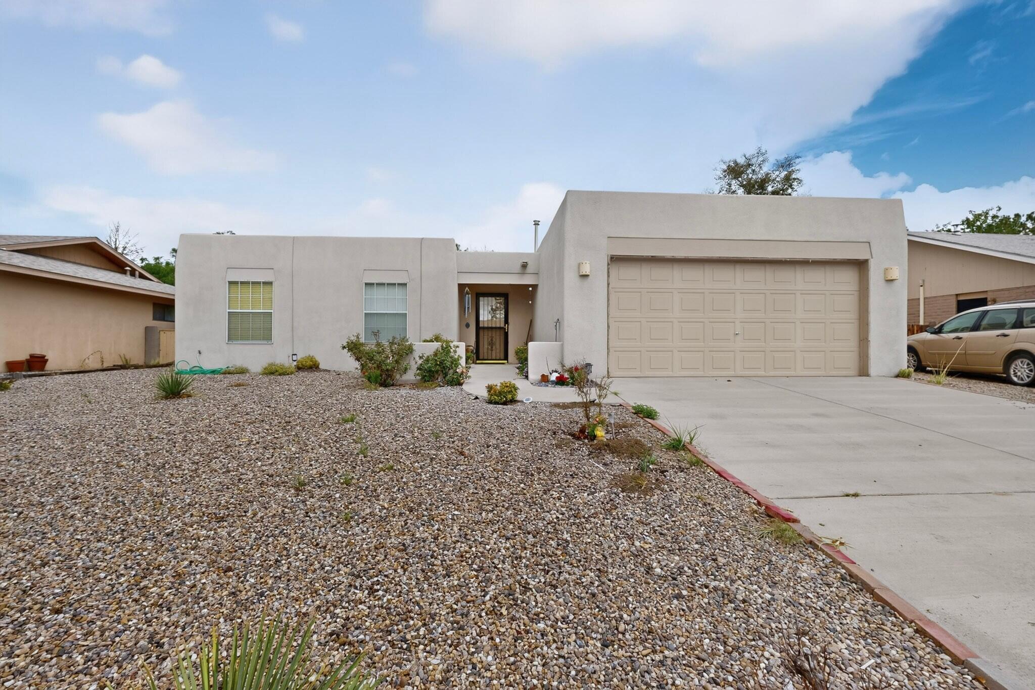 Single-story stucco home with a large garage, gravel landscaping, and a wide concrete driveway.