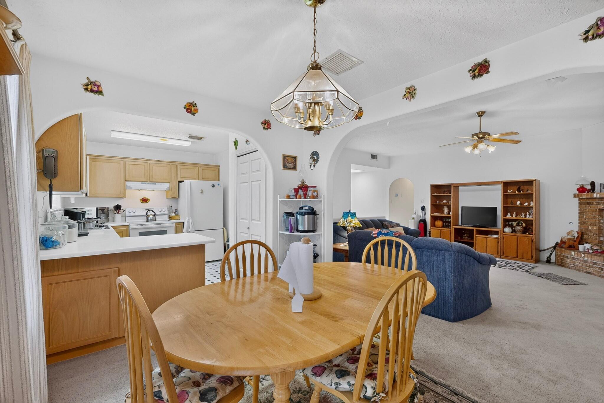 Open-plan kitchen and living room with a wood dining table, blue sofas, and brick fireplace.