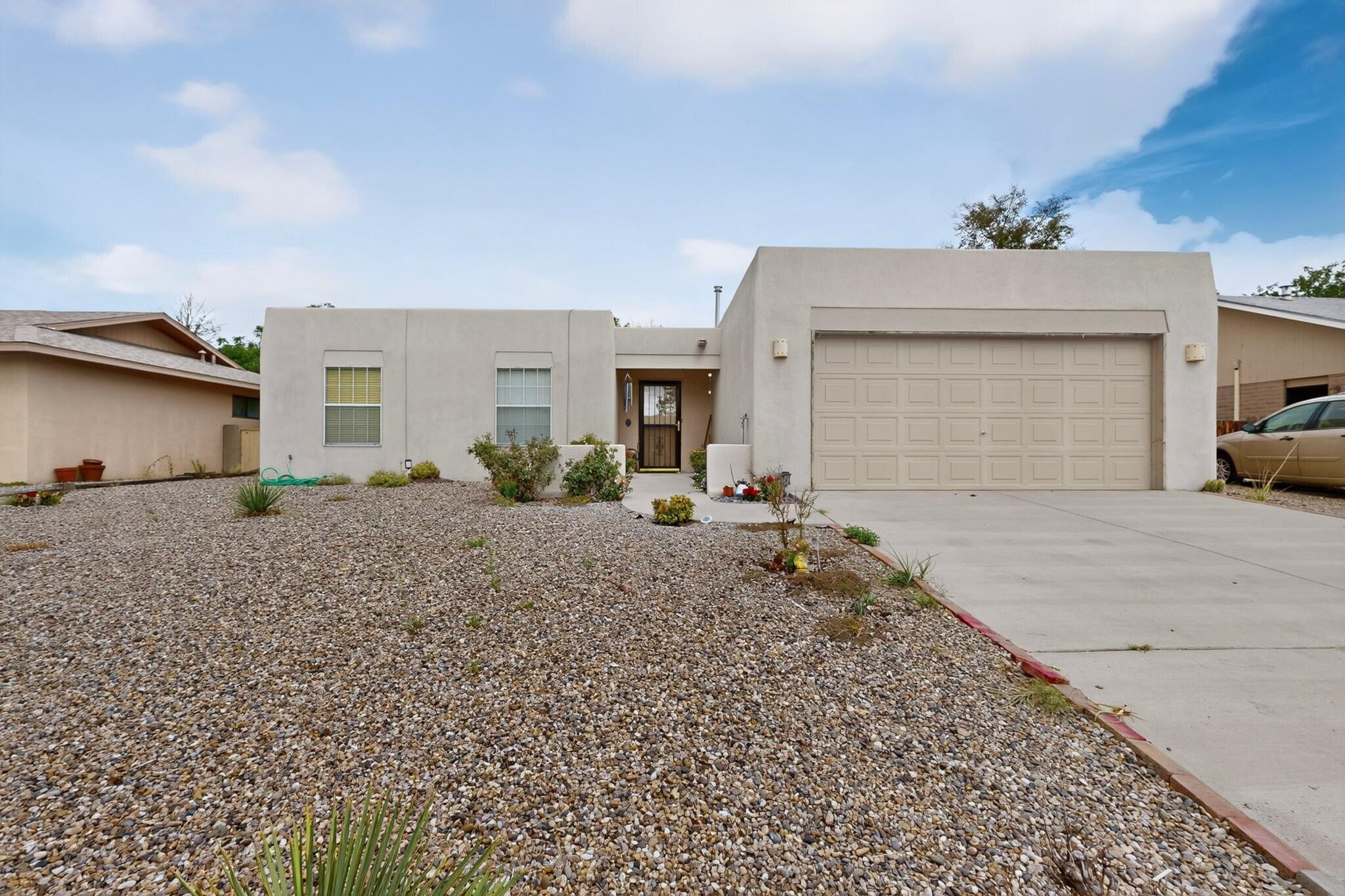 Single-story stucco home with a large garage and gravel front yard with sparse desert plants.