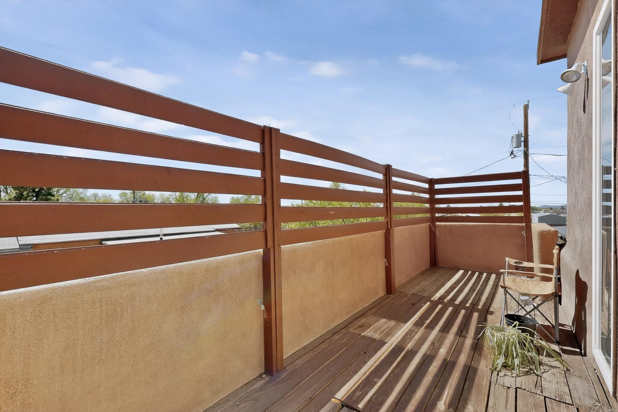 Narrow balcony with a reddish-brown slat privacy fence, weathered deck boards, and a folding chair.