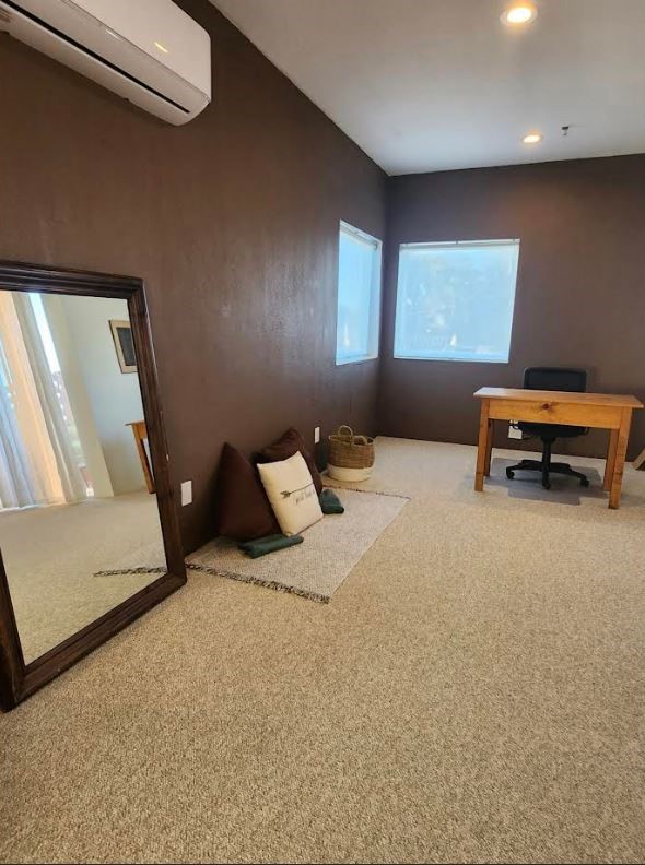 Carpeted home office with a wooden desk, two windows, and a wall-mounted mini-split air conditioner.