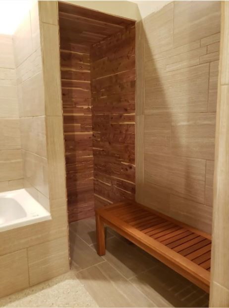 Tiled bathroom with a wood-paneled sauna alcove and slatted bench beside a bathtub.