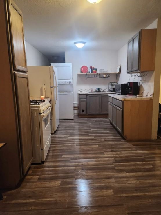 Kitchen with wood-tone cabinets, a gas stove, stacked washer and dryer, and plank flooring.