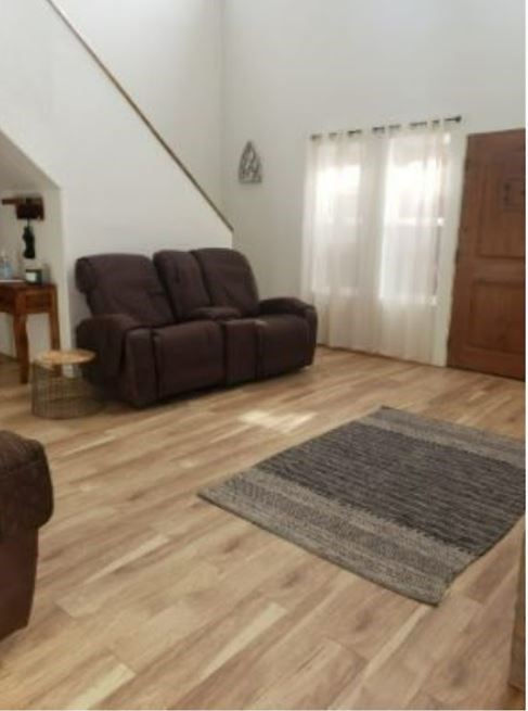 Living room with a dark reclining loveseat, gray area rug, and light wood flooring.