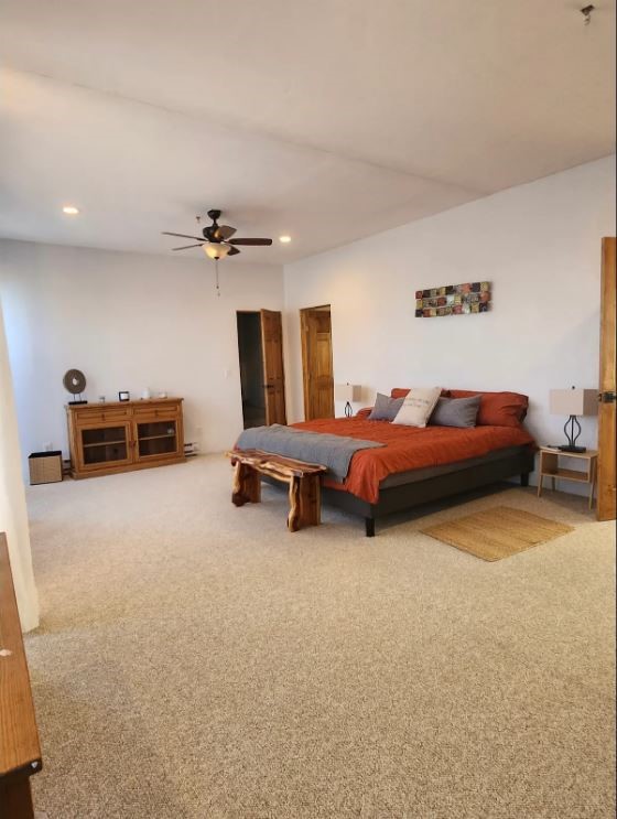 Furnished bedroom with rust-orange bedding, a wooden bench, beige carpet, and ceiling fan.