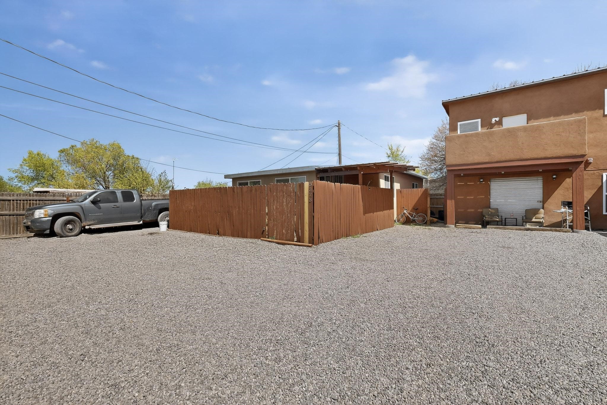 Two-story stucco home with a covered patio, wooden privacy fence, and wide gravel yard.