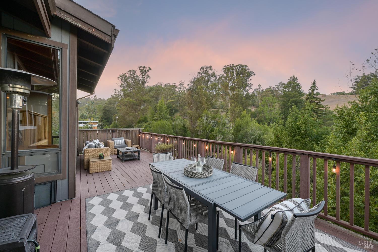 Outdoor deck with dining and lounge seating overlooking wooded hills at dusk.