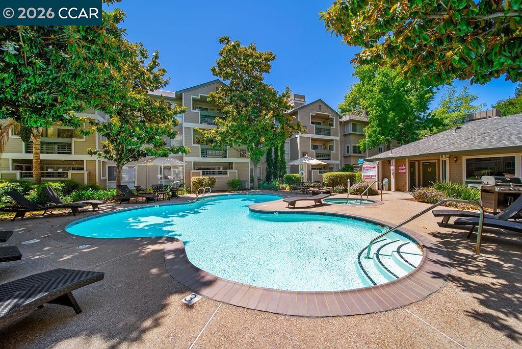 Apartment complex pool with a circular spa, lounge chairs, and landscaped courtyard.
