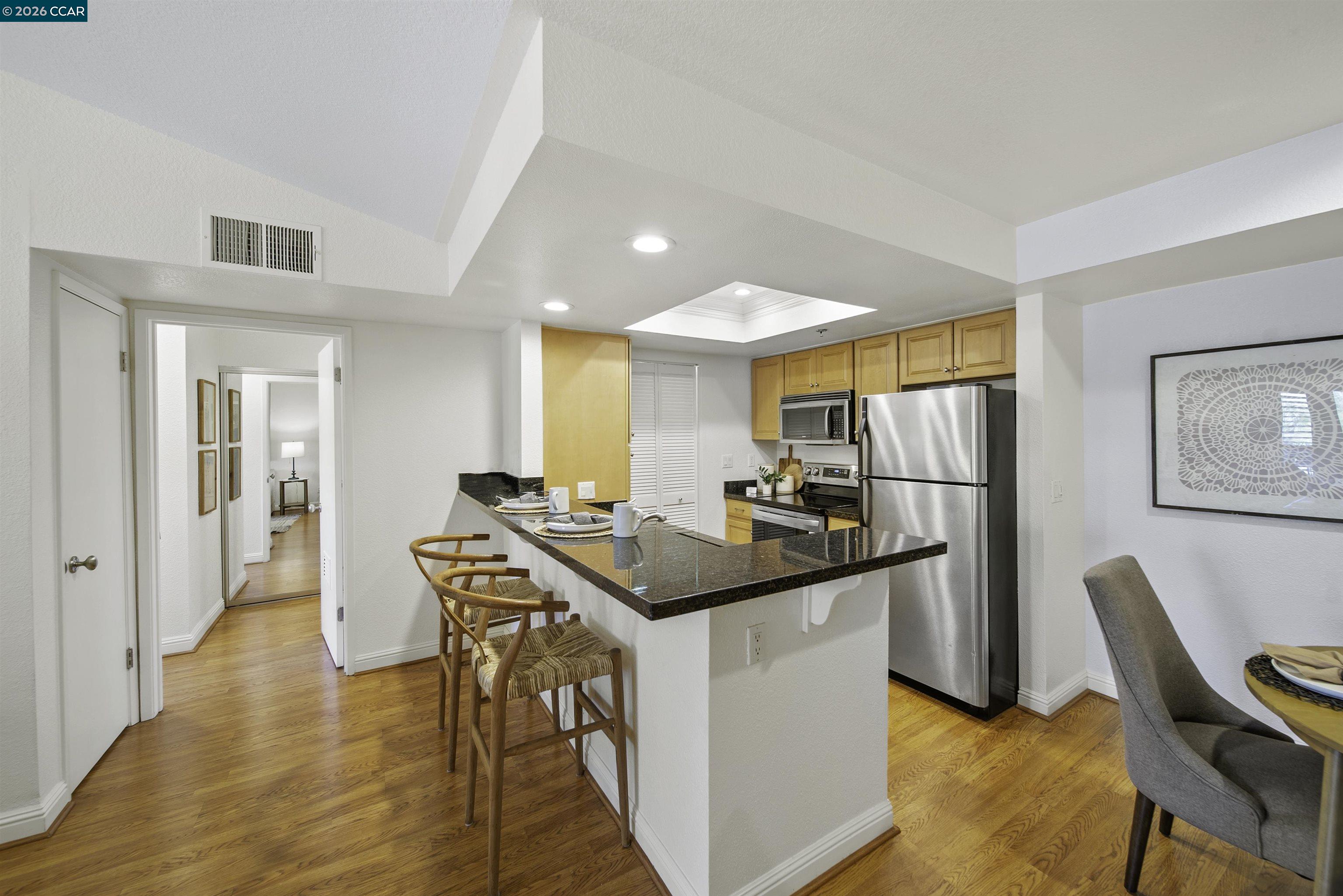 Kitchen with granite breakfast bar, stainless steel appliances, wood cabinets, and hardwood floors.