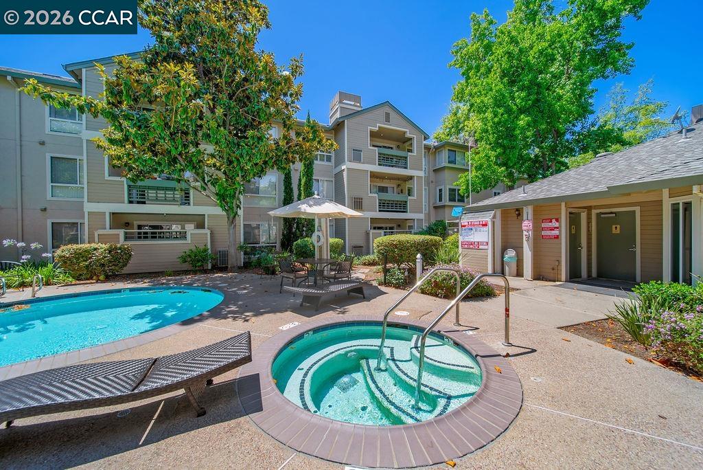 Apartment complex pool courtyard with a circular hot tub, lounge chairs, and mature trees.