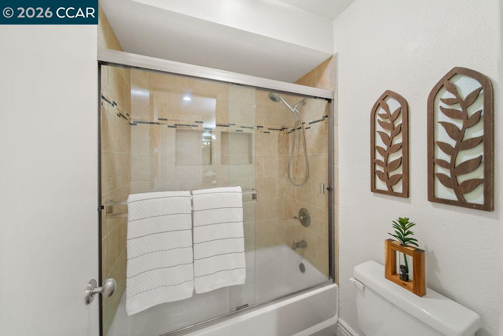 Bathroom with a glass-enclosed tub and shower, beige tile, and white towels.