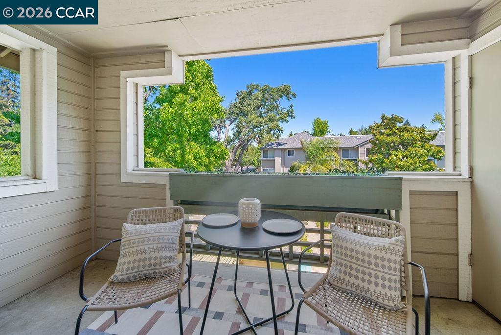 Covered balcony with woven chairs and a round table overlooking trees and neighboring homes.
