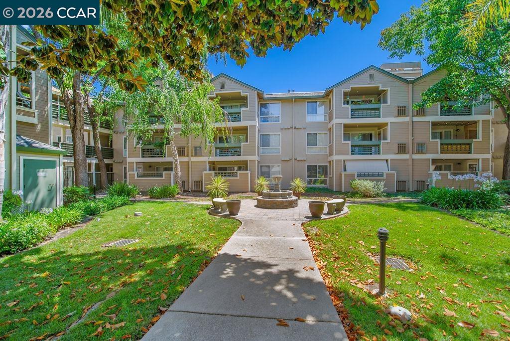 Apartment building surrounding a landscaped courtyard with a fountain and paved walkway.
