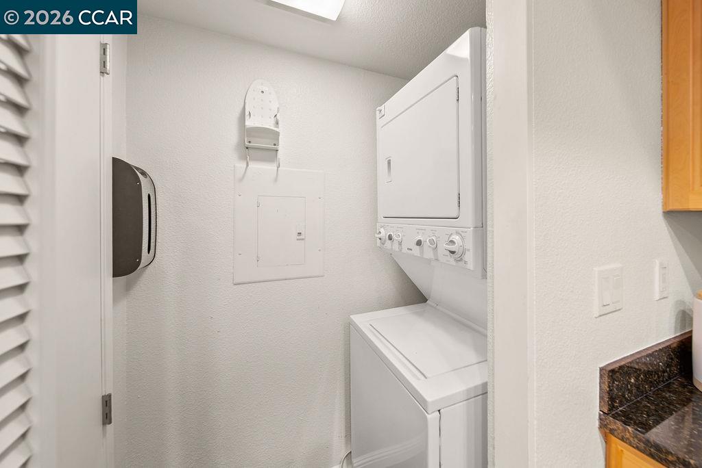 Laundry closet with a white stacked washer and dryer and a wall-mounted ironing board.