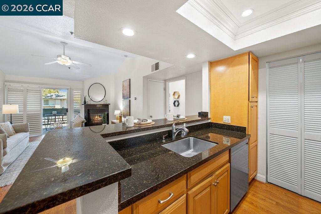 Kitchen with dark granite counters, a double-basin sink, and honey-colored cabinets opening to a living area.