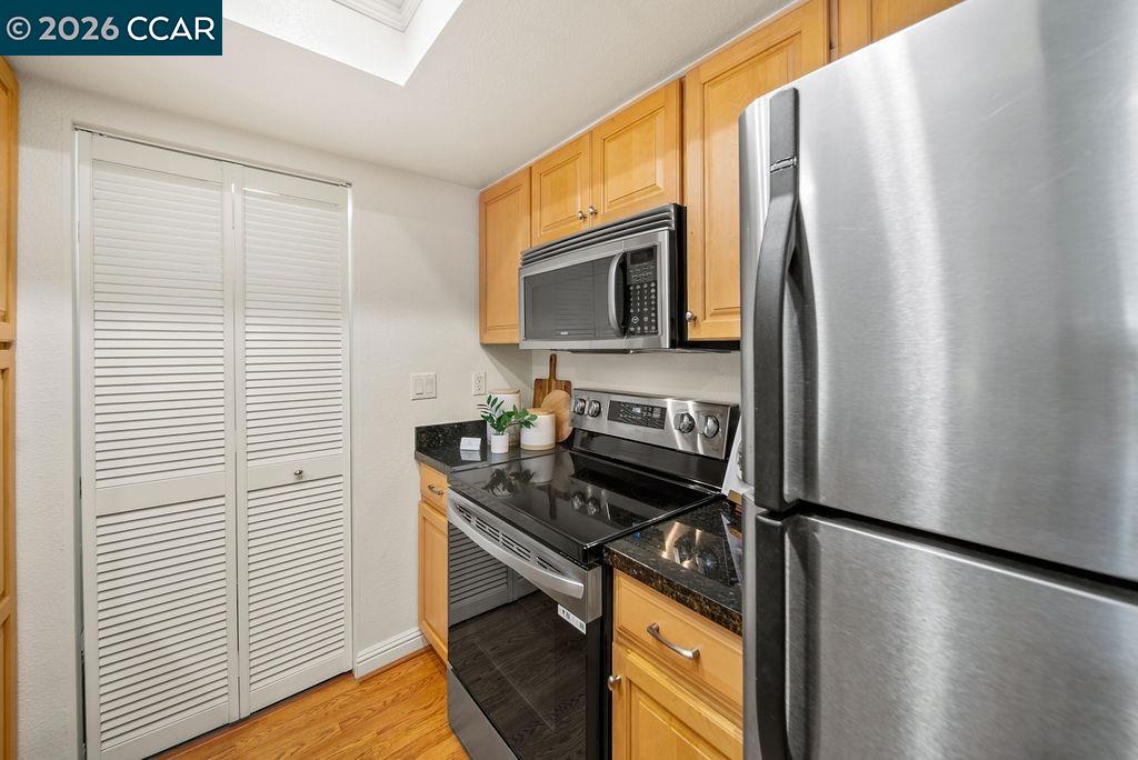 Kitchen with wood cabinets, dark countertops, and stainless steel appliances beside white louvered doors.