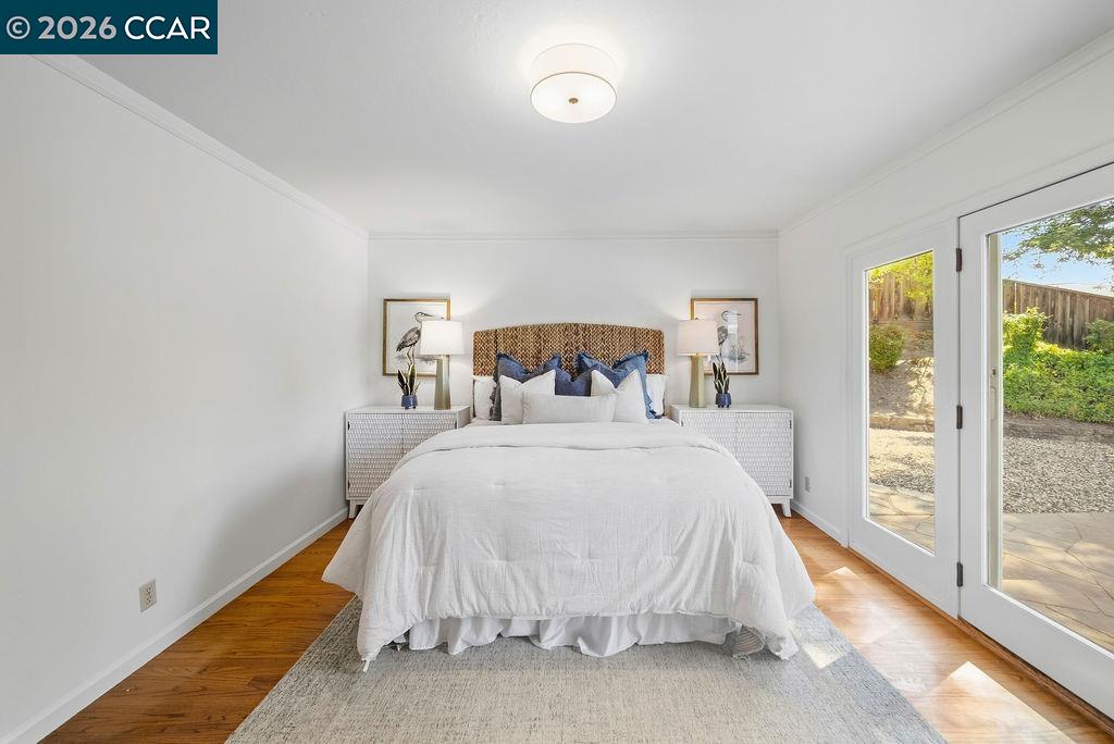 Staged bedroom with a white bed, woven headboard, hardwood floors, and glass doors to a patio.