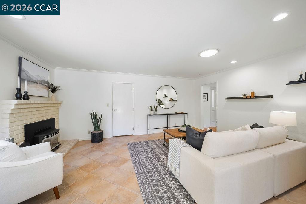 Staged living room with white sofas, tan tile floors, and a white brick fireplace.