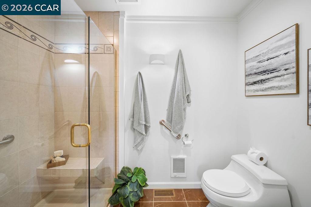 Bathroom with a glass-enclosed tiled shower, white toilet, grab bars, and framed abstract art.