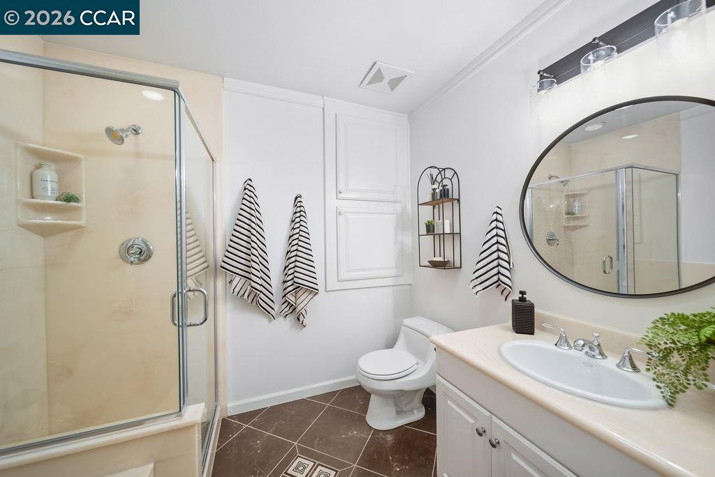 Bathroom with glass-enclosed shower, white vanity, oval mirror, and striped towels.