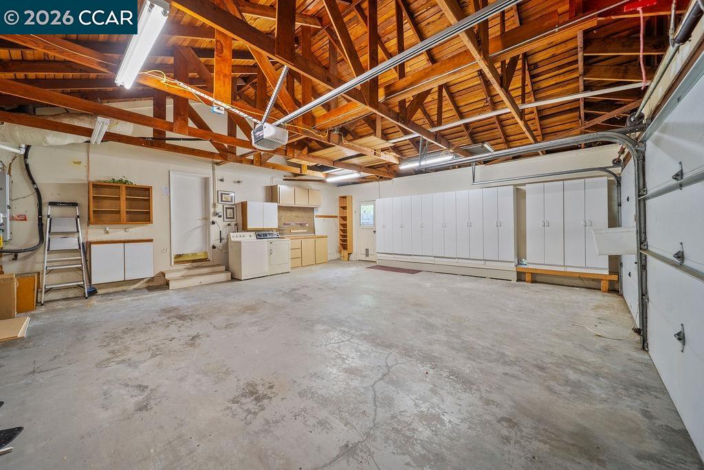Spacious garage with exposed wooden rafters, white storage cabinets, and a laundry area.