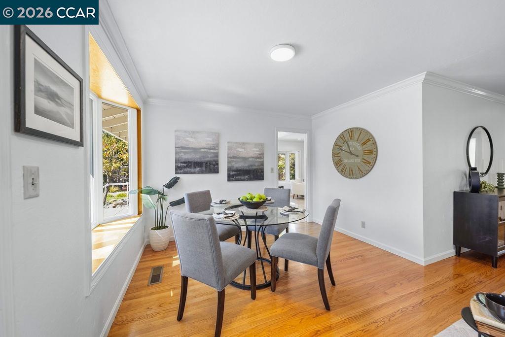 Dining room with a round glass table, gray chairs, hardwood floors, and a large sunny window.