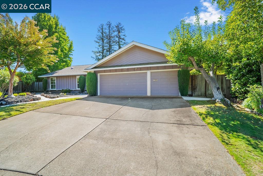 Single-story home with a two-car garage, broad driveway, landscaped lawn, and mature trees.