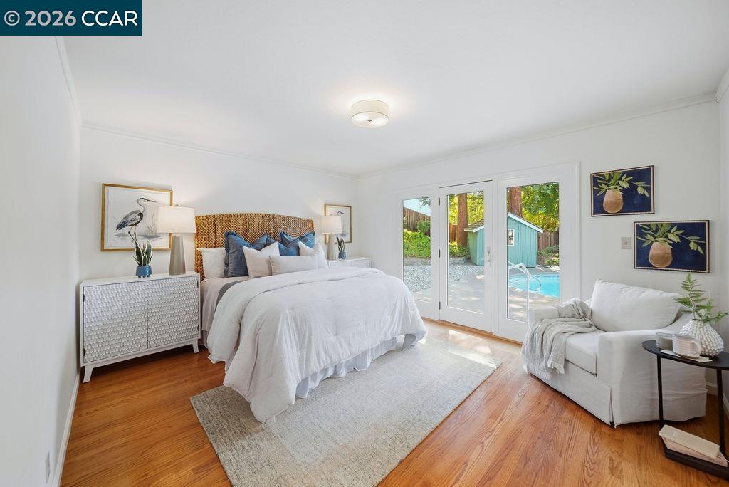 Staged bedroom with a large bed, hardwood floors, and French doors overlooking a backyard pool.