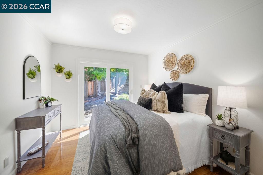 Staged bedroom with gray bedding, a glass door to the yard, and hardwood floors.