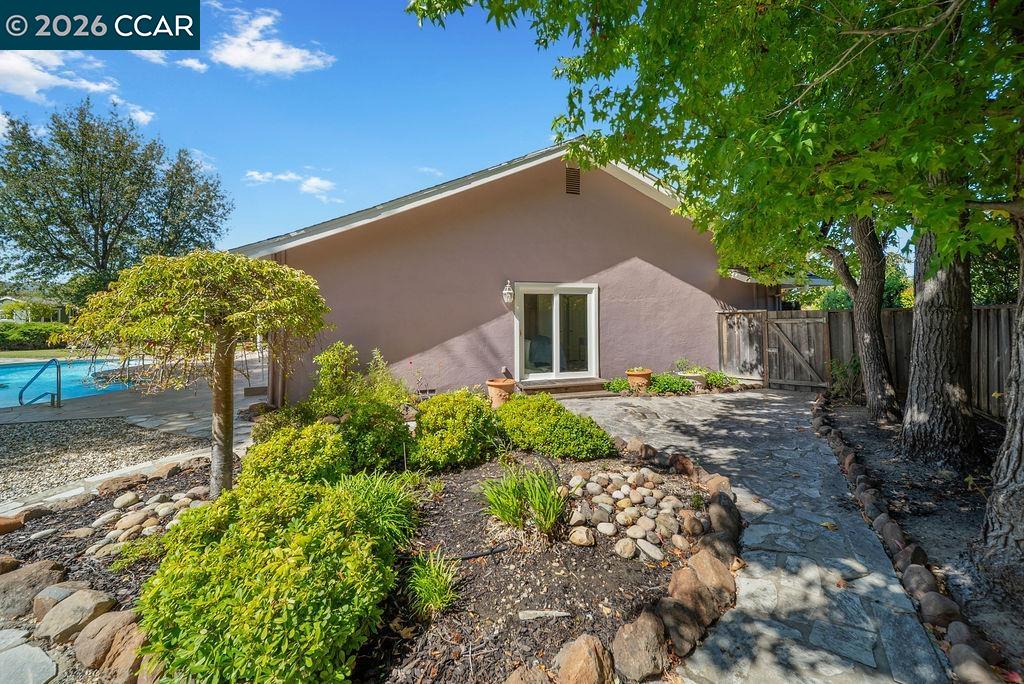 Home’s rear patio and garden with a swimming pool, stone path, and mature shade trees.
