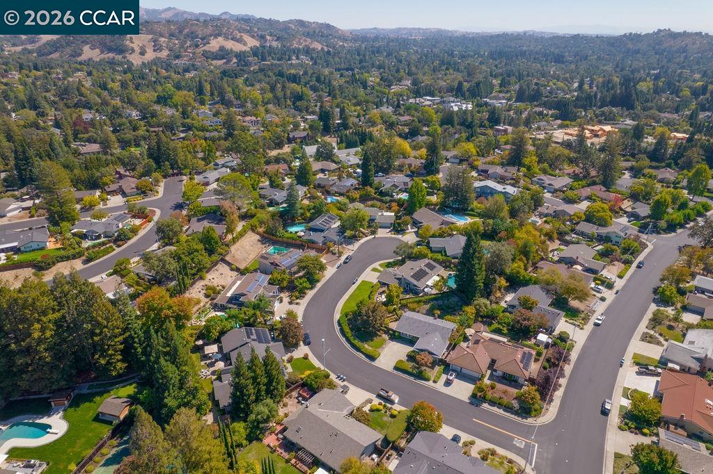 Aerial view of a leafy neighborhood with winding streets and wooded hills in the distance.