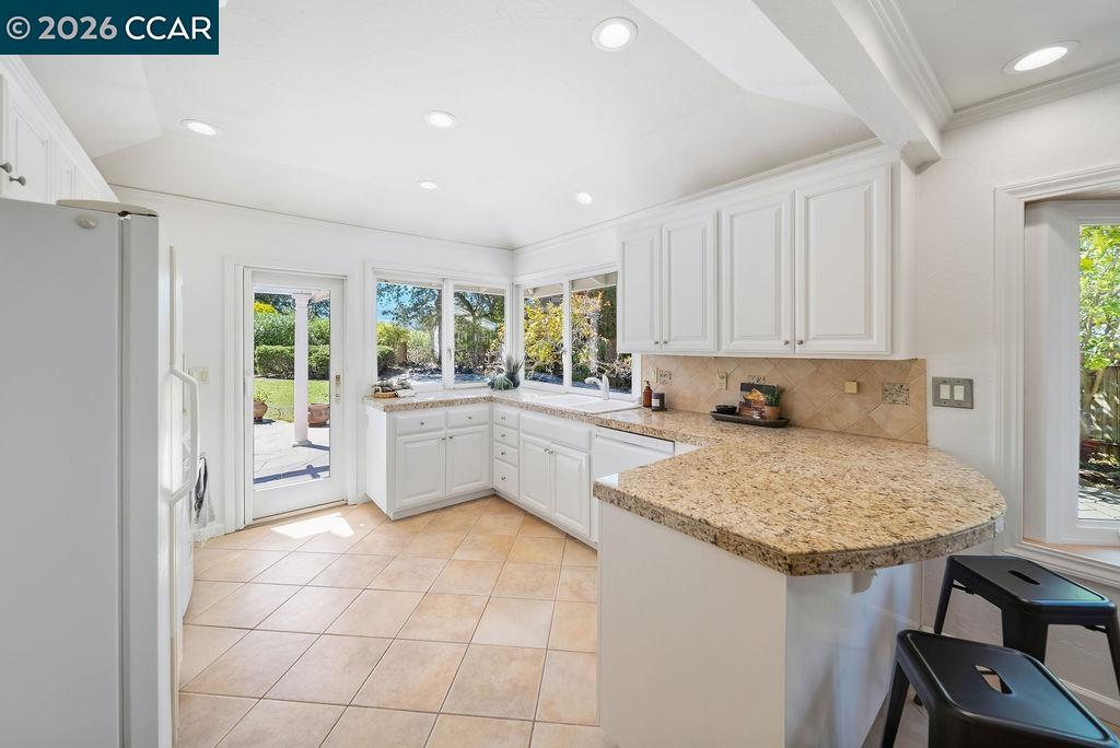 White kitchen with granite peninsula, tan tile floors, and windows overlooking a garden.