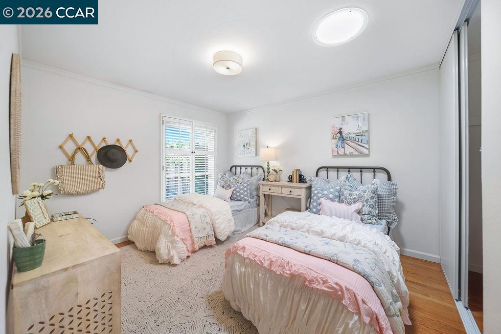 Bedroom with two twin beds, pale pink bedding, dark metal headboards, and plantation shutters.