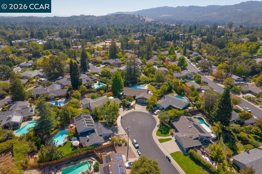 Aerial view of homes and swimming pools around a cul-de-sac, with wooded hills beyond.