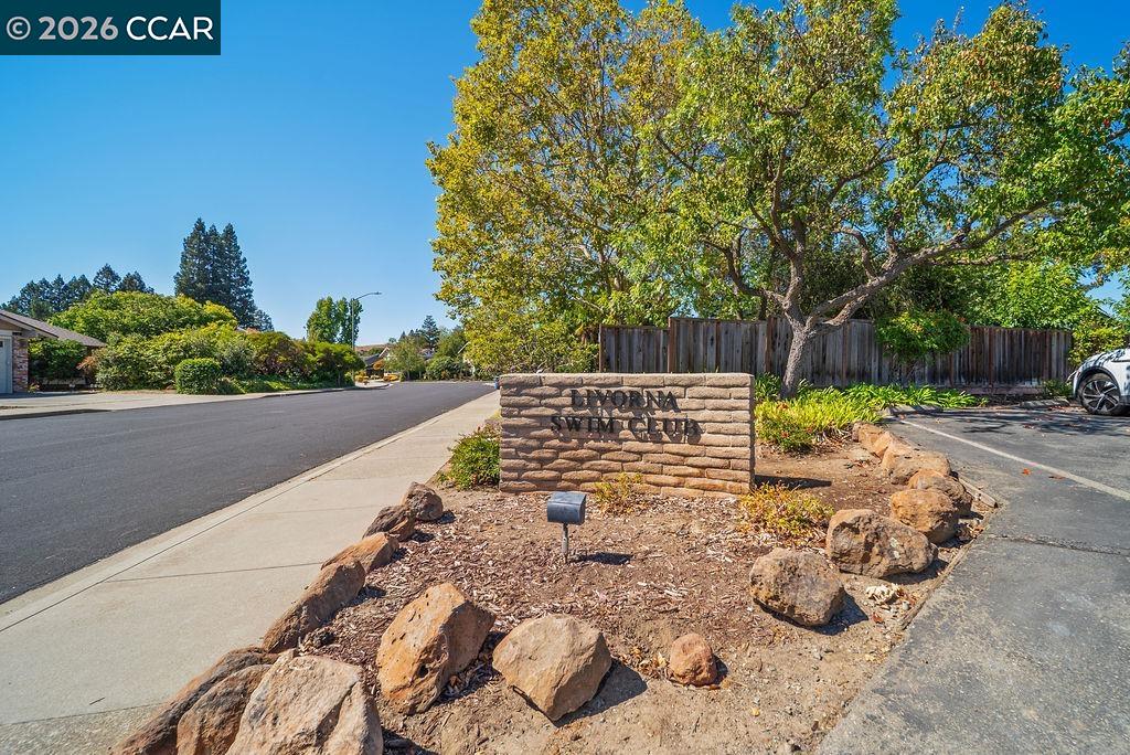 Landscaped neighborhood entrance with a stone sign beside a residential street.