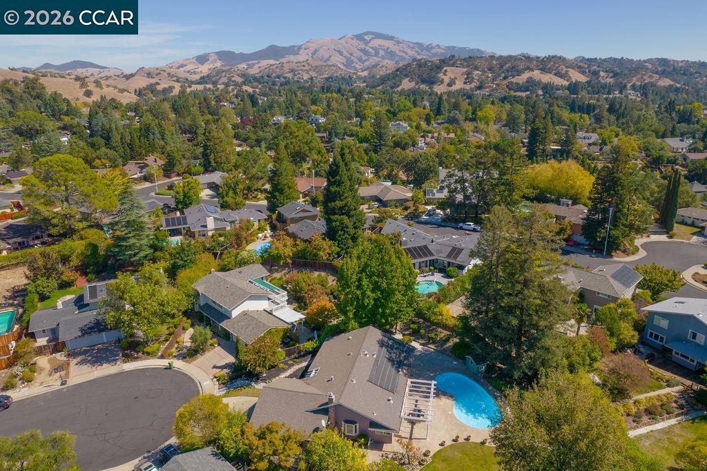 Aerial view of a home with a pool in a tree-lined neighborhood beneath distant hills.