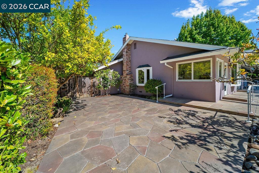 Single-story home with mauve siding and a spacious flagstone courtyard bordered by mature trees.