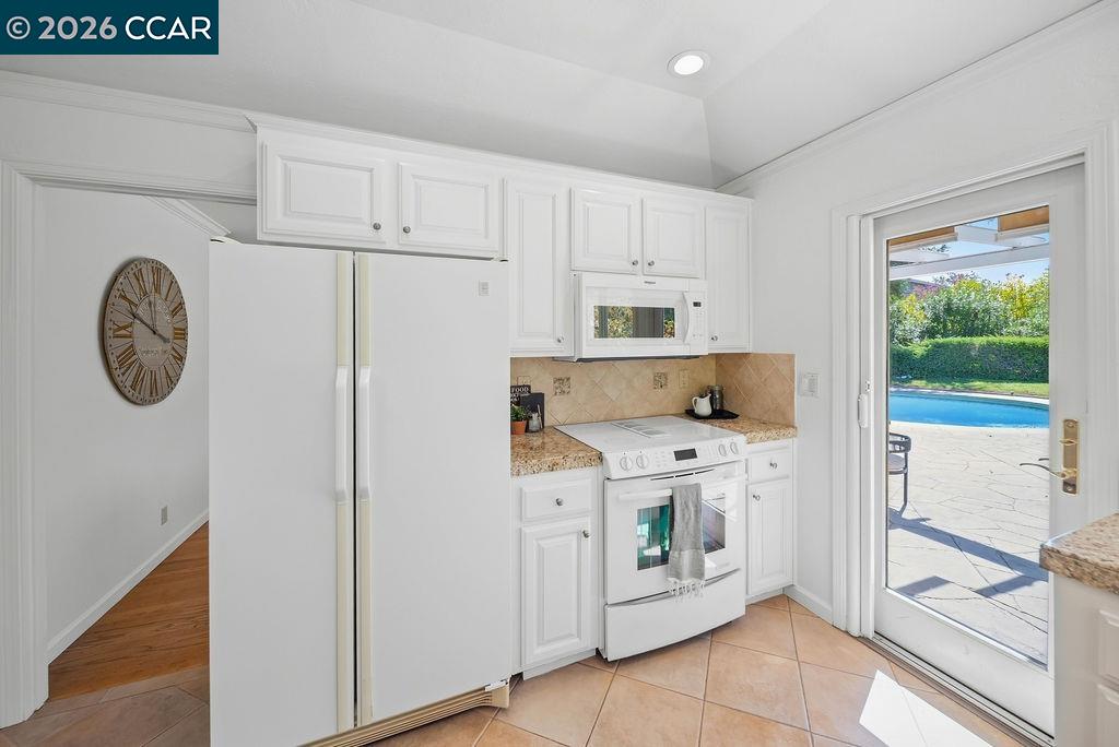 White kitchen with paneled cabinets and appliances, opening through a glass door to a pool patio.