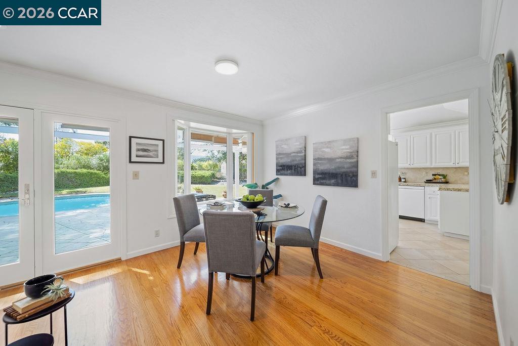 Dining area with a glass table, hardwood floors, and doors overlooking a swimming pool.