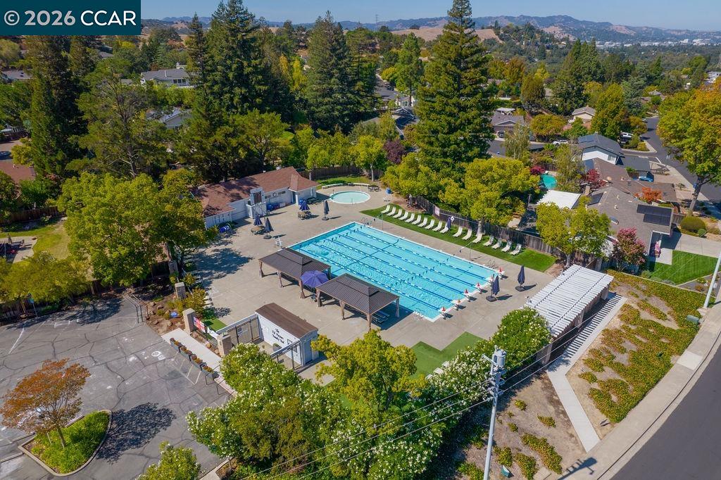 Aerial view of a neighborhood swimming pool with shaded seating and rolling hills beyond.