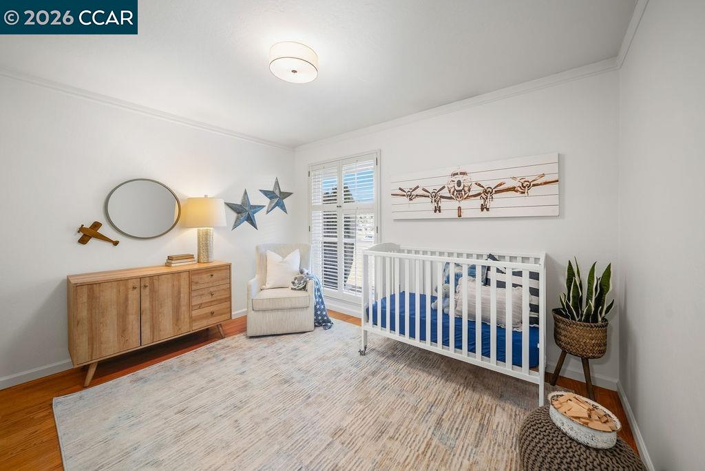 Nursery with a white crib, blue bedding, wooden dresser, and armchair beside shuttered windows.