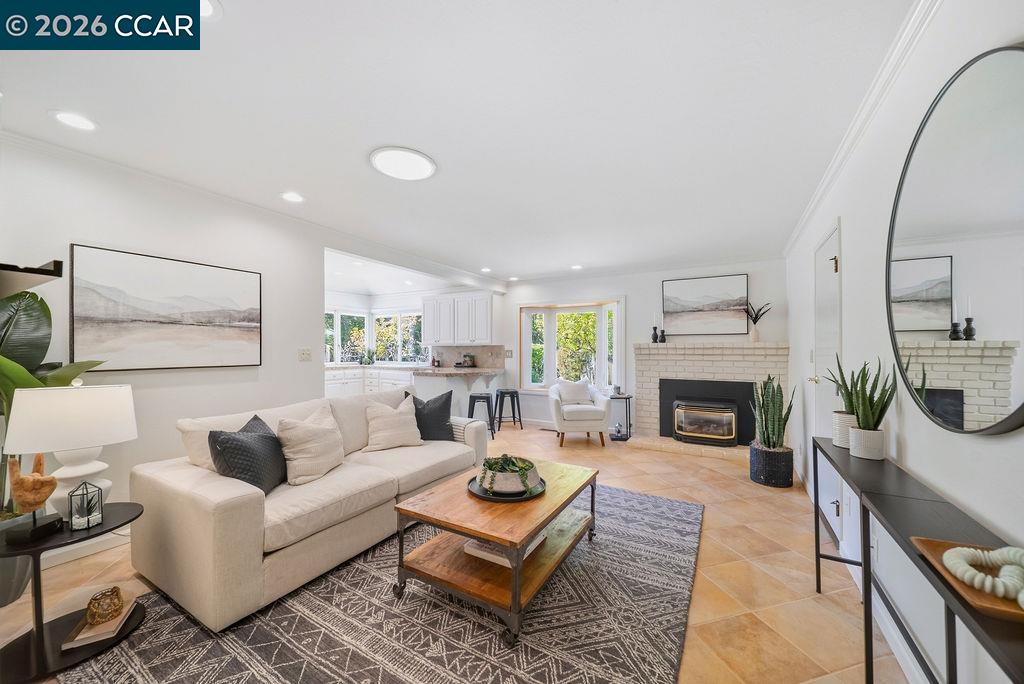 Staged living room with a cream sectional, white brick fireplace, and open kitchen.