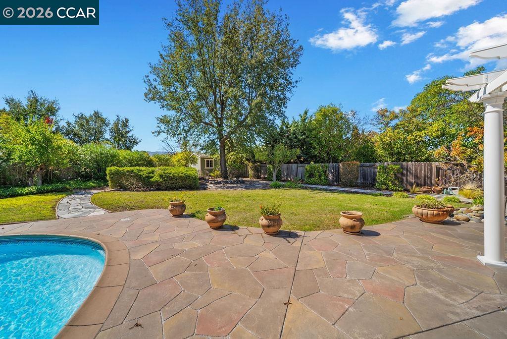 Backyard pool and flagstone patio beside a lawn, with potted plants and mature trees.