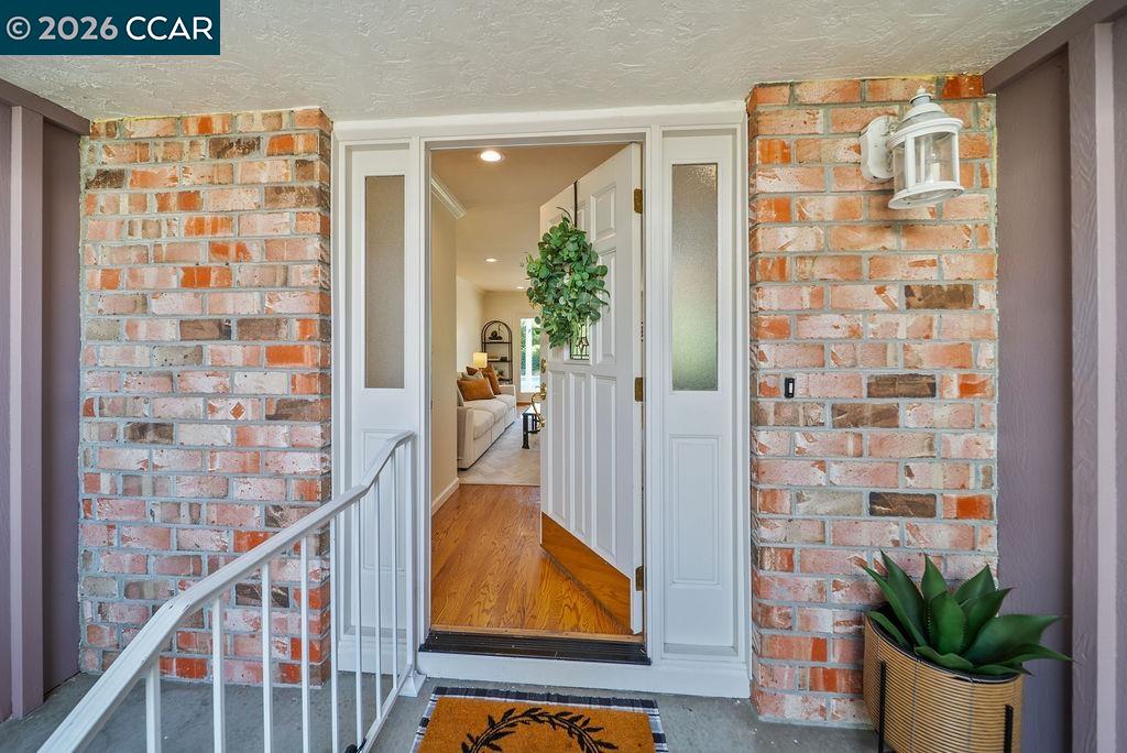 Brick front entrance with open white doors, a covered porch, and a potted plant.