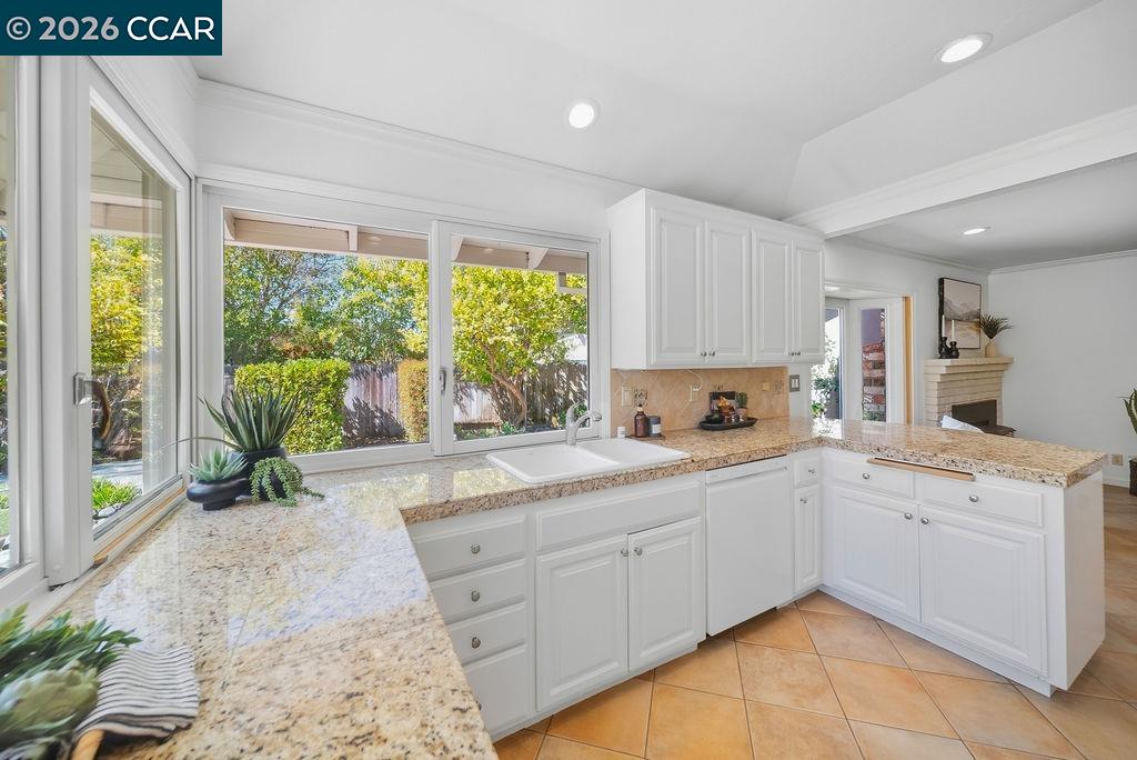 Bright kitchen with white cabinetry, granite counters, and large windows overlooking greenery.