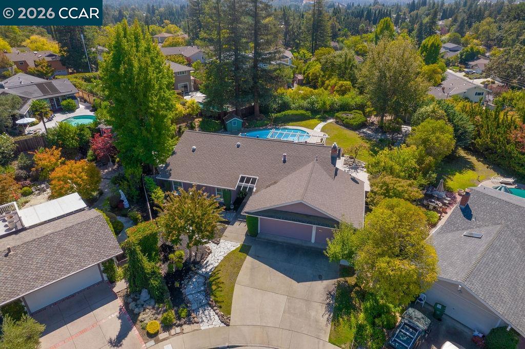 Aerial view of a home with a backyard pool, broad driveway, and mature trees.