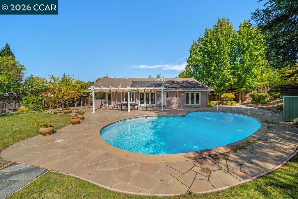 Backyard swimming pool beside a stone patio and covered seating area.