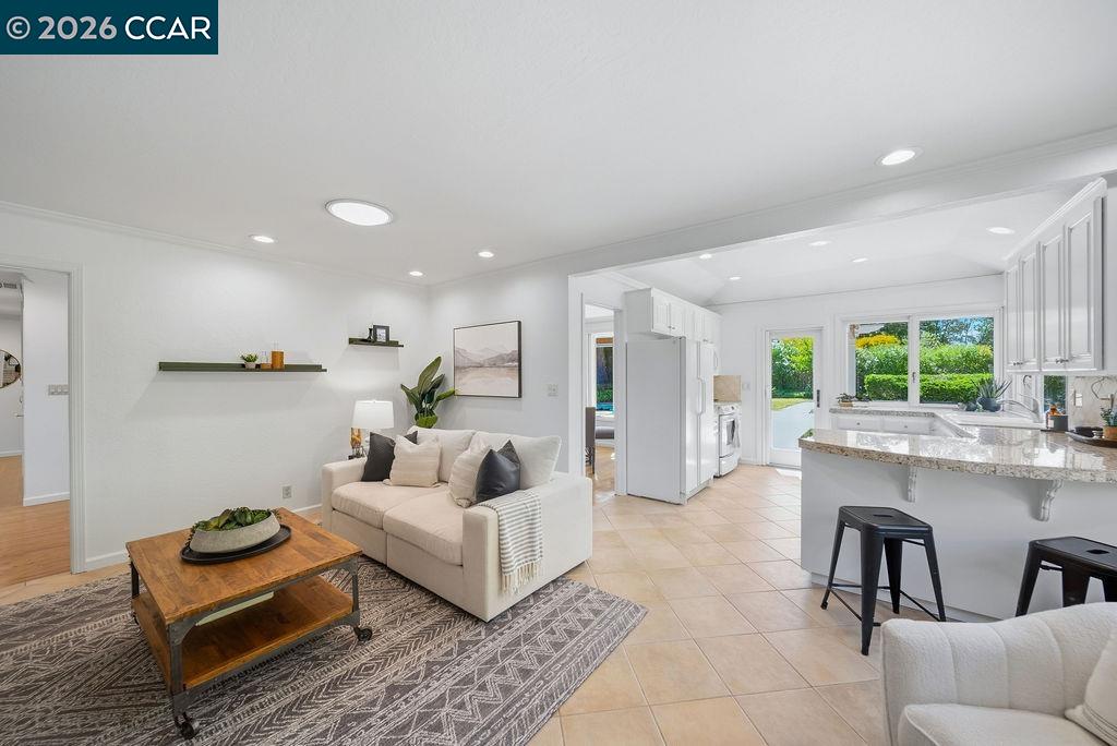 Open-plan living room and kitchen with a cream sofa, patterned rug, and island facing garden windows.