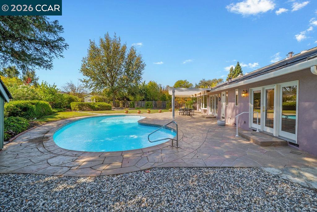 Backyard pool with curved stone patio beside a single-story home and landscaped lawn.