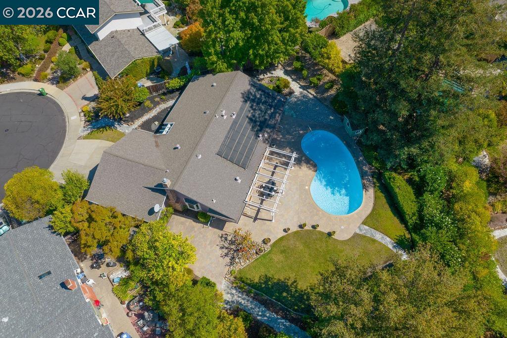 Aerial view of a home with a curved pool, patio pergola, and rooftop solar panels.